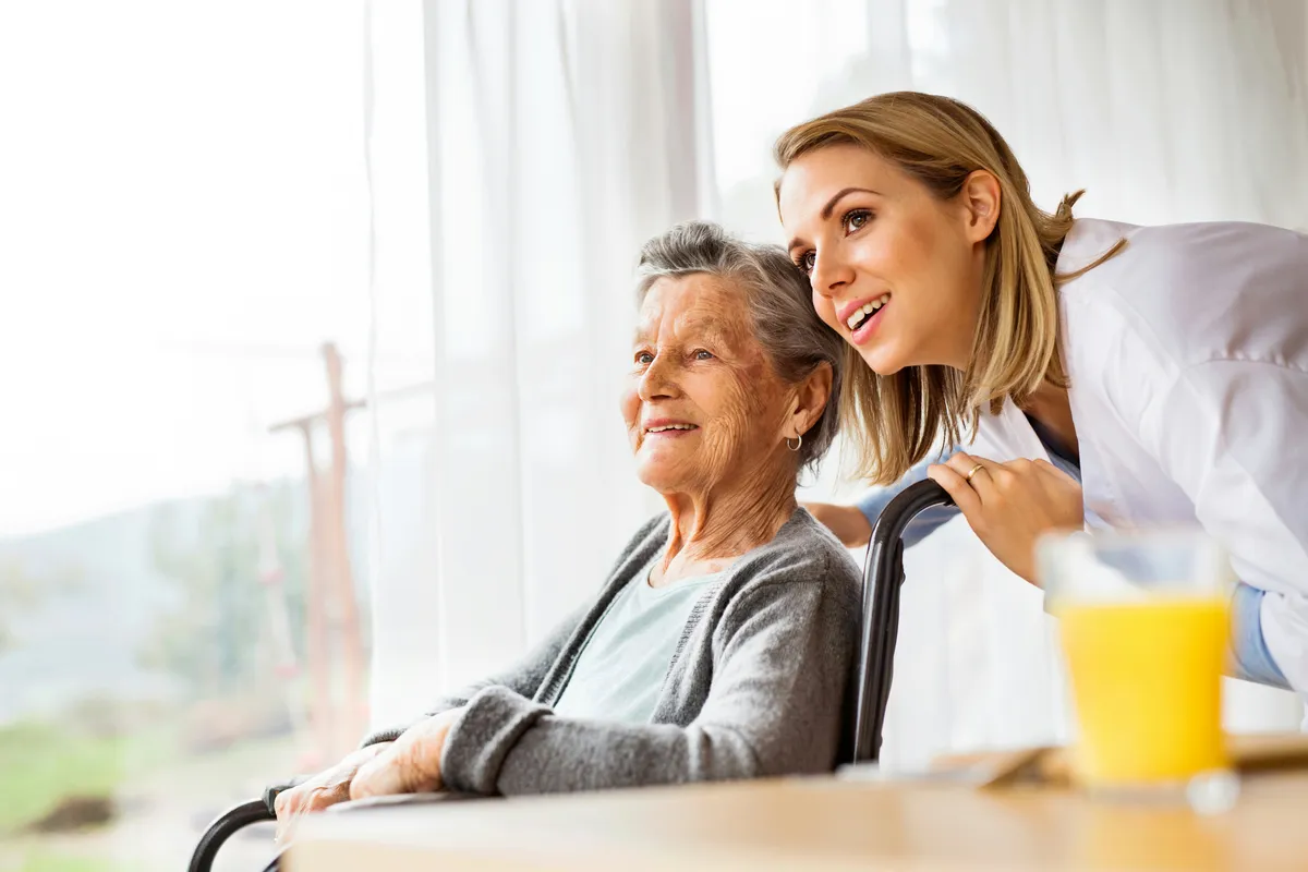 Healthcare professional smiling with an elderly patient looking out a window